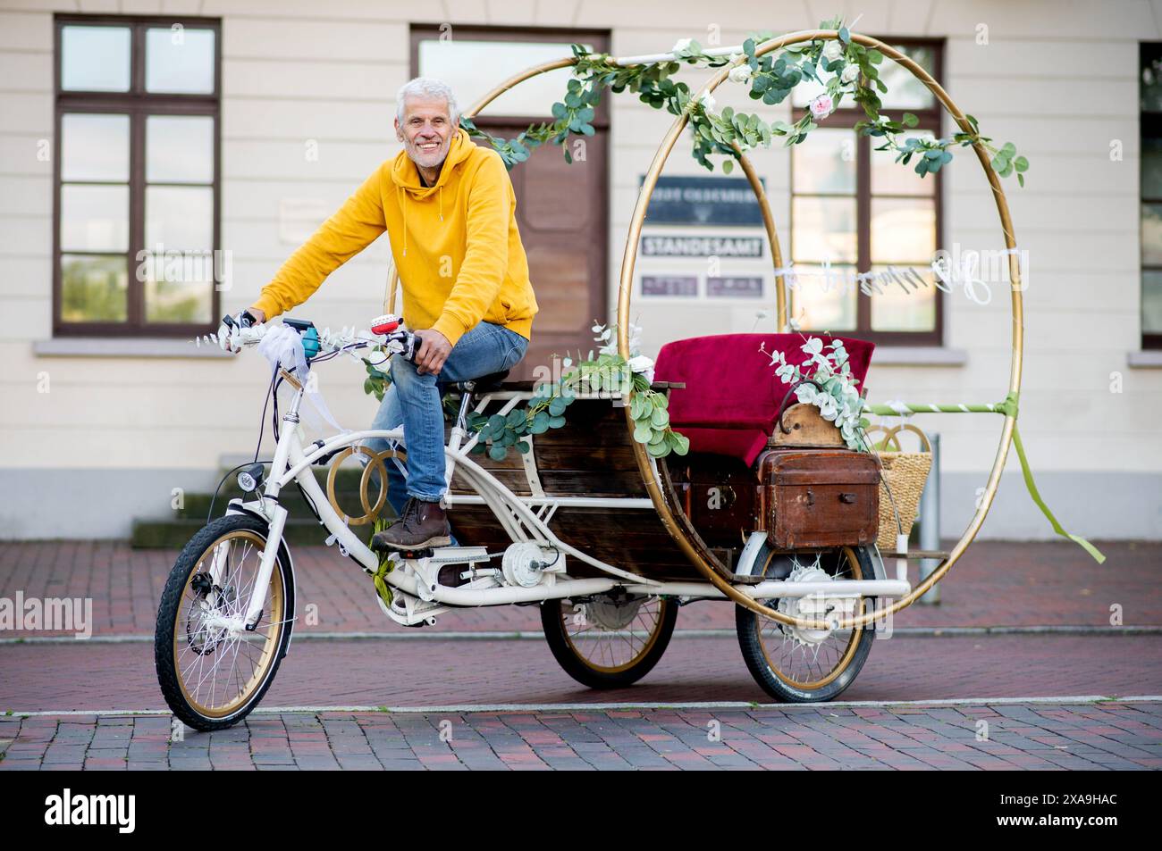 Oldenburg, Germania. 29 maggio 2024. L'artista del metallo Michael Olsen si trova con la sua bicicletta da sposa di fronte all'ufficio del registro della città di Oldenburg a Pferdemarkt. Olsen ha costruito la bicicletta con due anelli sovradimensionati nel 2022 e da allora ha continuato a svilupparla. Offre alle coppie nuziali giri in bicicletta il giorno del loro matrimonio. Crediti: Hauke-Christian Dittrich/dpa/Alamy Live News Foto Stock