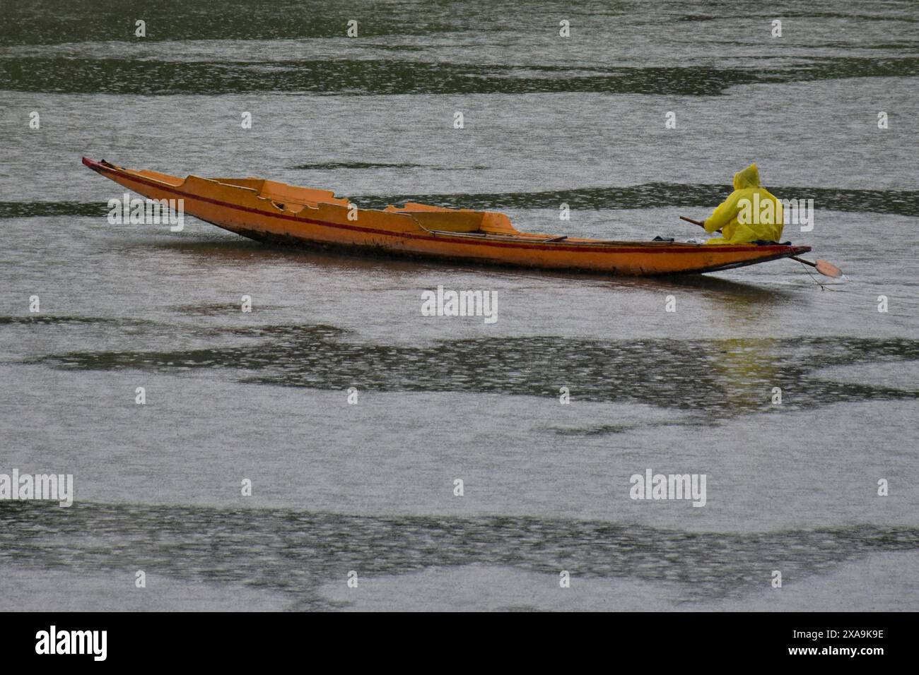 Un uomo che indossa un impermeabile infila la sua barca attraverso il fiume Jehlum durante le precipitazioni a Srinagar, la capitale estiva di Jammu e Kashmir. Foto Stock