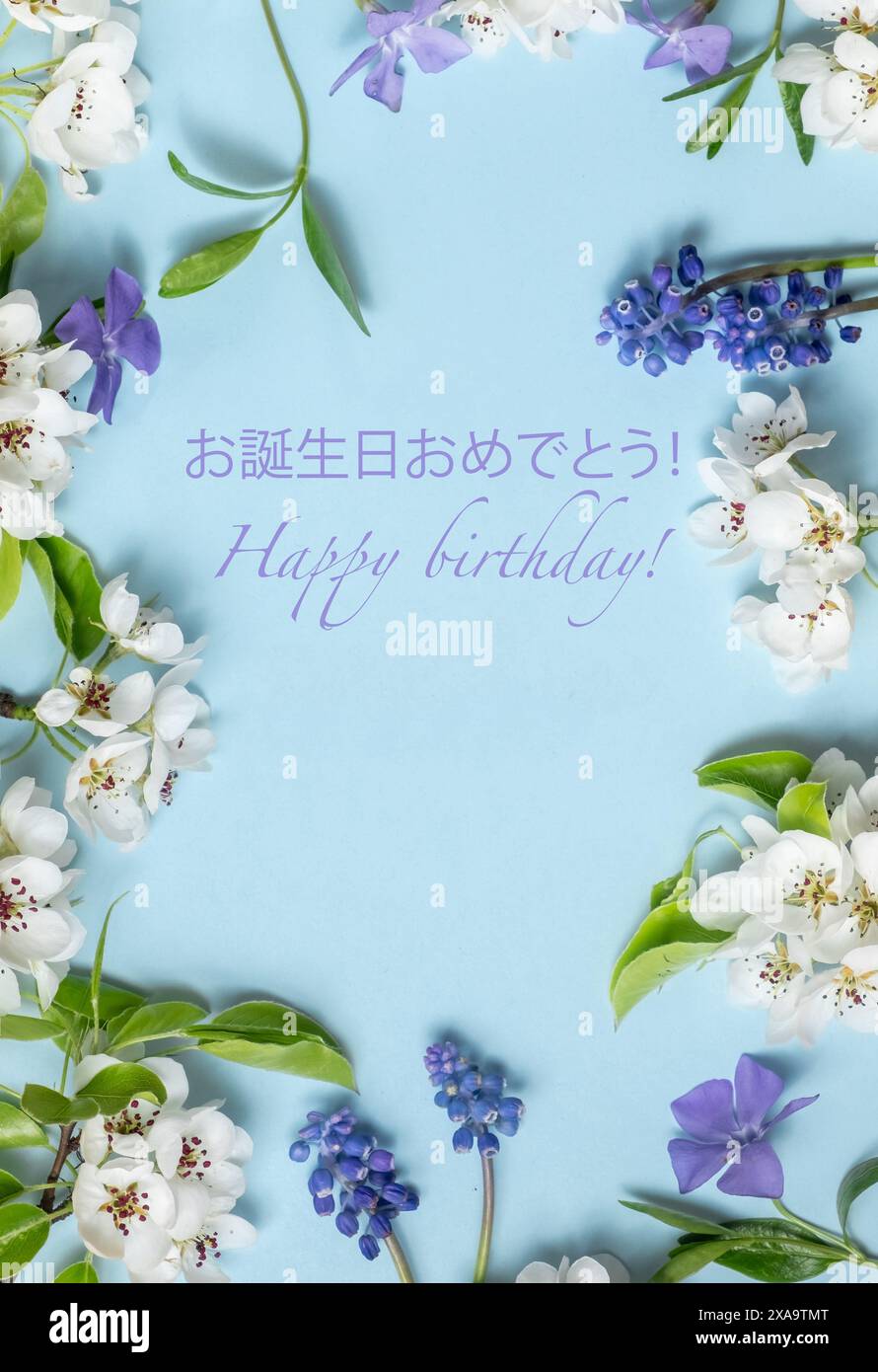 Biglietto di auguri di buon compleanno in giapponese e inglese e fiori freschi di primavera colorati su un morbido sfondo blu. Foto estetica, disposizione piatta Foto Stock