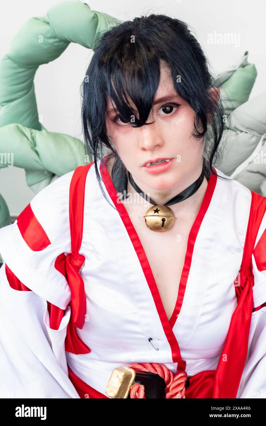 Una cosplayer donna con un vestito bianco e rosso e una campana intorno al collo in posa con un arco e una freccia Foto Stock
