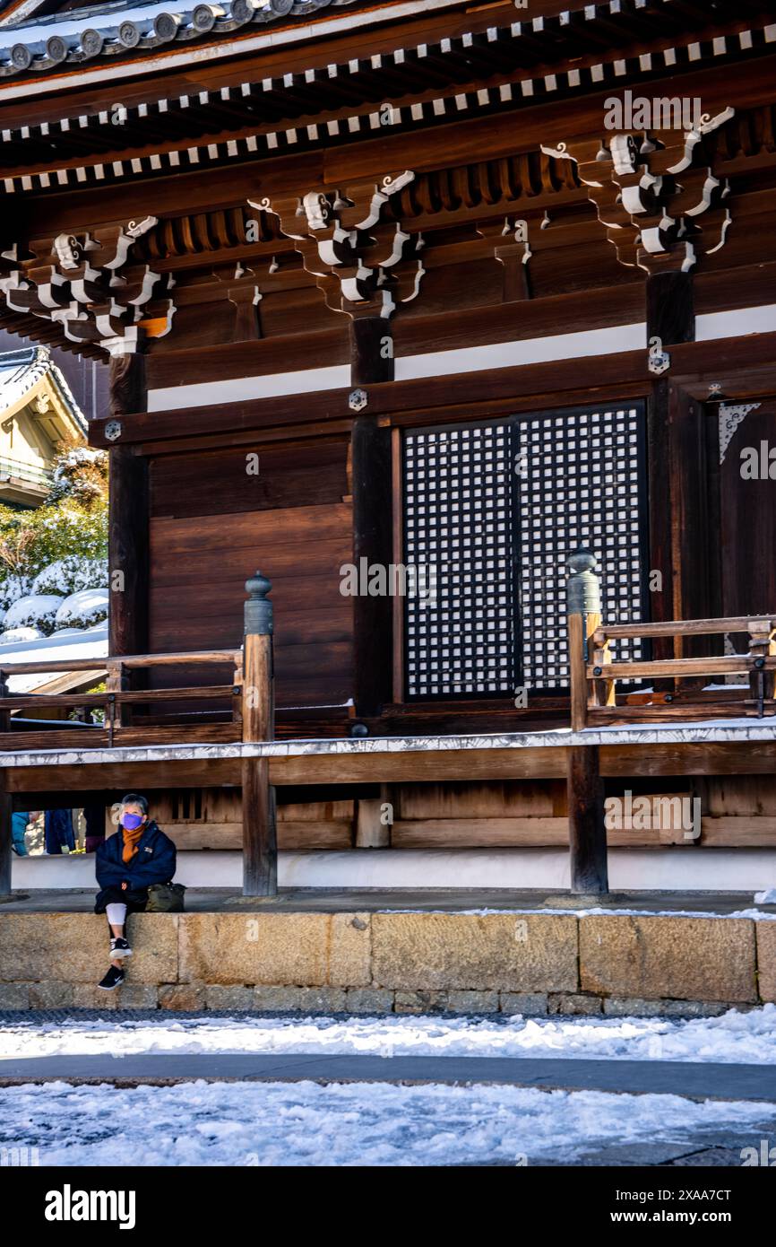 Donna giapponese mascherata seduta su una piattaforma coperta di neve nell'antico complesso sacro del tempio buddista Kiyomizudera a Kyoto, in Giappone Foto Stock