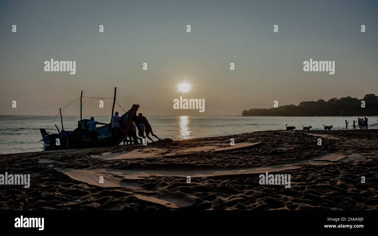 Un gruppo di persone si gode il tramonto sulla spiaggia accanto a una barca Foto Stock