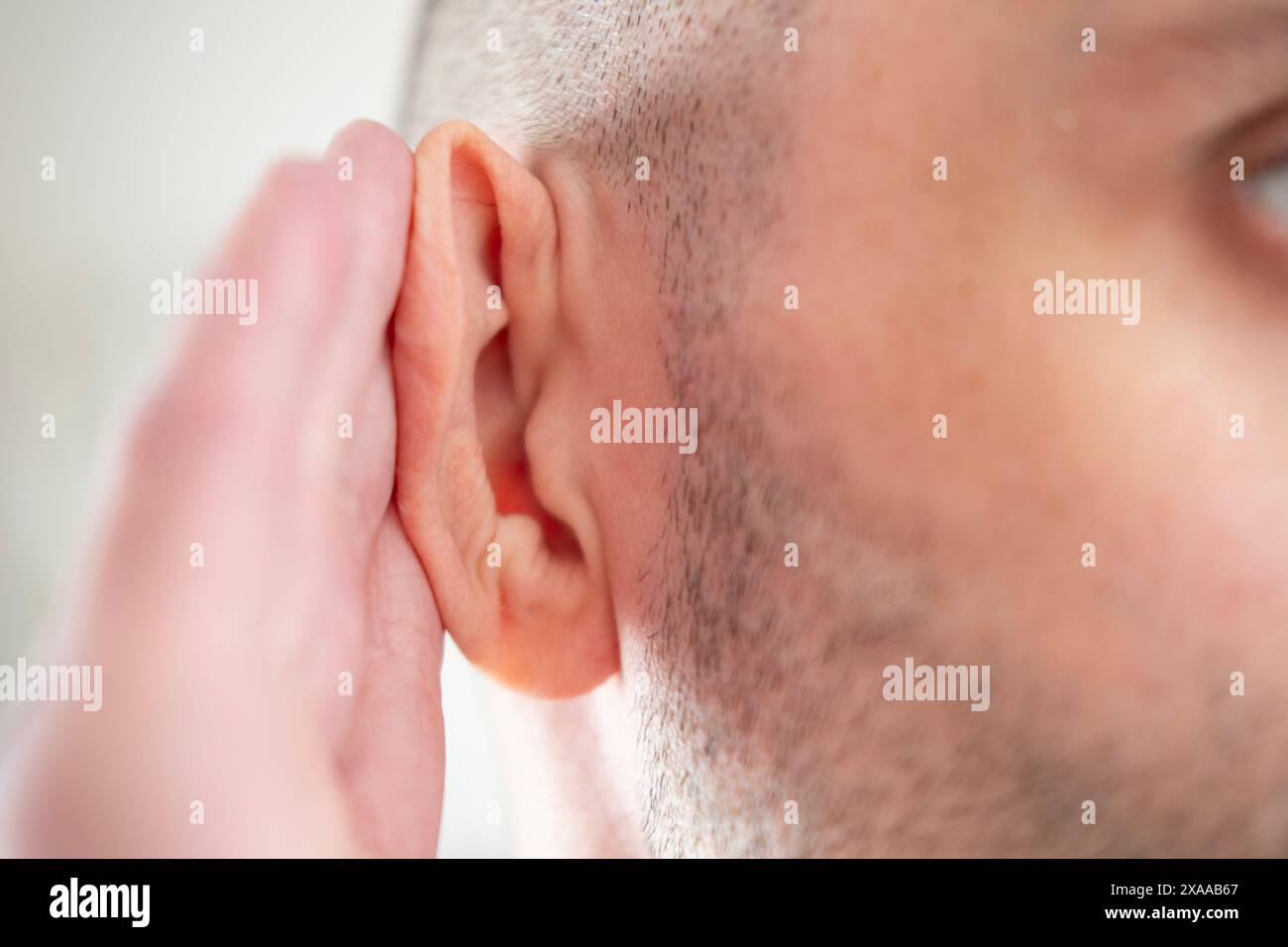 Il giovane si aggrappa all'orecchio nel dolore, soffre di mal di orecchio grave, perdita dell'udito, disagio all'orecchio, test dell'udito, otite media acuta, trattamento e cura Foto Stock