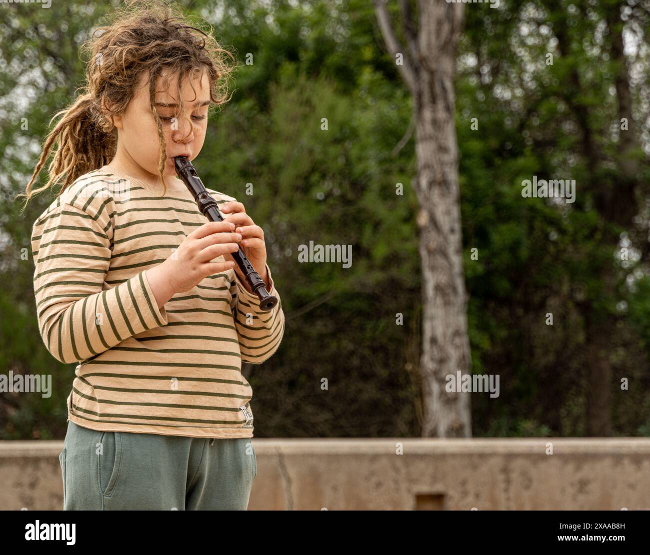 Immergiti nell'armonia della natura da ragazzo con lunghi capelli biondi e dreadlocks crea melodie magiche con il suo flauto tra gli alberi. Una scena di puro Foto Stock