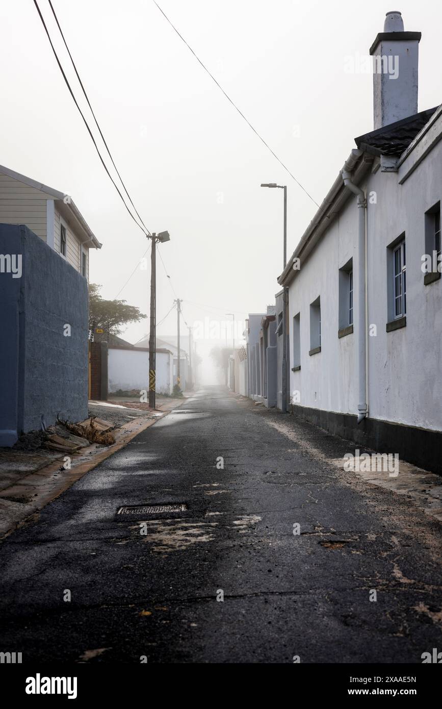 Una strada nebbiosa a Strand, Sud Africa, fiancheggiata da edifici tranquilli e linee elettriche Foto Stock