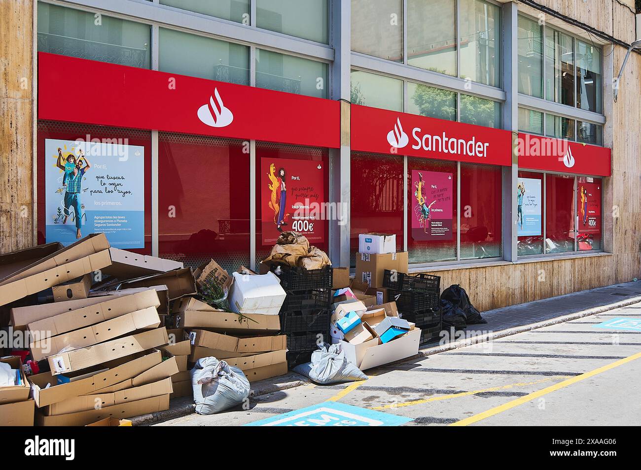 Sitges, Barcellona, Spagna - 5 giugno 2024: Facciata della banca di Santander con segni rossi e un mucchio di scatole di cartone sul marciapiede raffiguranti il contrasto urbano. Foto Stock