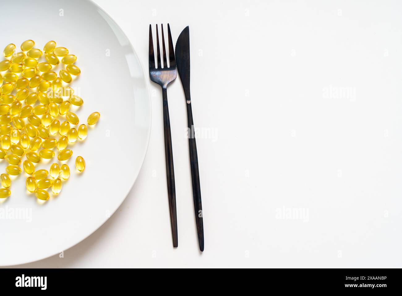 Molte pillole di olio di pesce giallo chiaro, omega 3 su un piatto bianco con forchetta e coltello su sfondo chiaro. Primo piano. Copia spazio. Foto di alta qualità Foto Stock