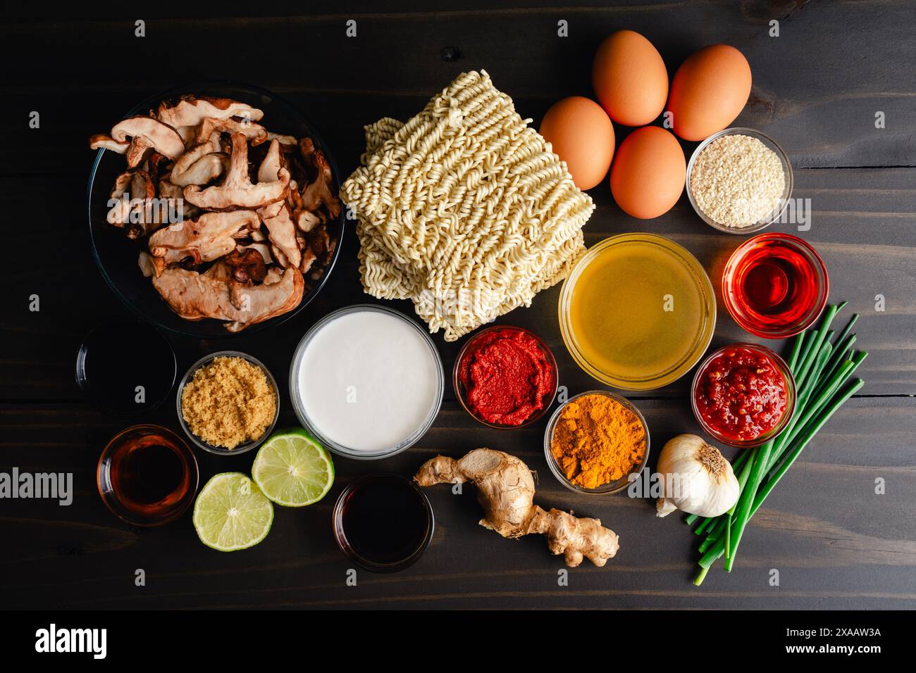 Ingredienti speziati al curry di cocco Ramen su un tavolo di legno: Tagliatelle di ramen istantanee, funghi shiitake, pasta di curry e altri ingredienti Foto Stock