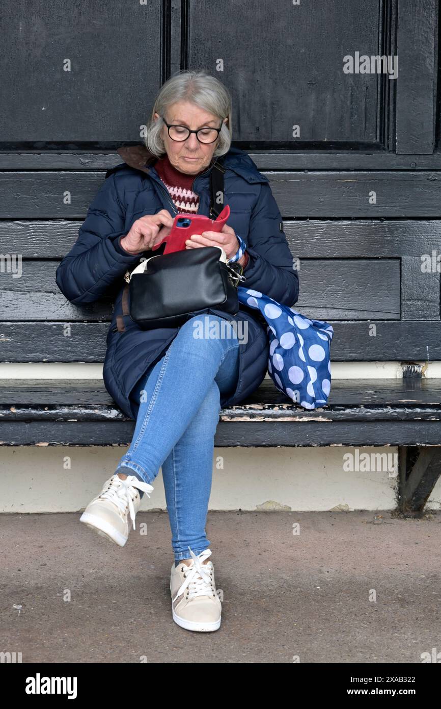 donna anziana in pensione che usa il telefono cellulare Foto Stock