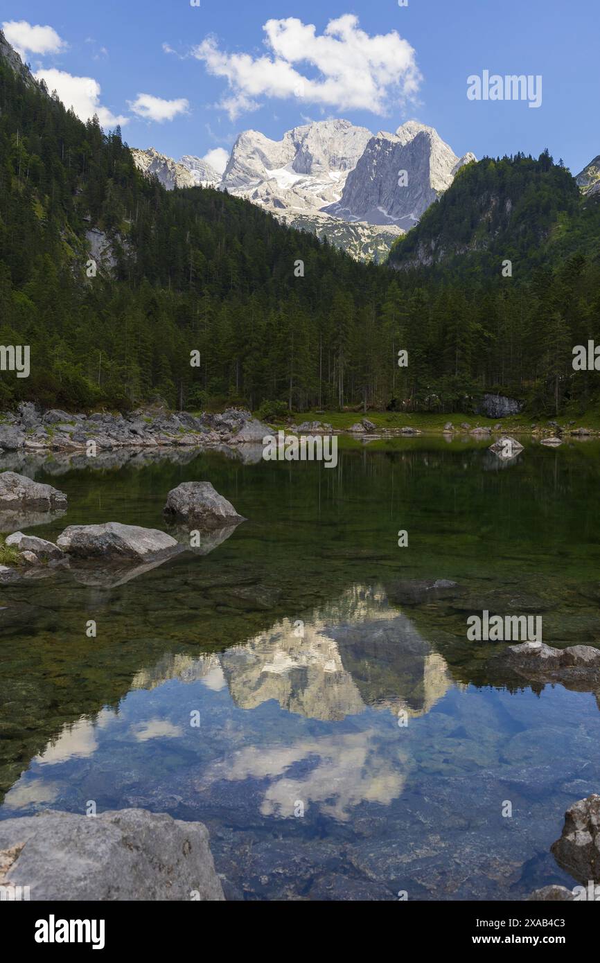 Fotografia di un piccolo lago alpino circondato dalle Alpi austriache settentrionali con riflessi sulle montagne Hoher Dachstein Foto Stock