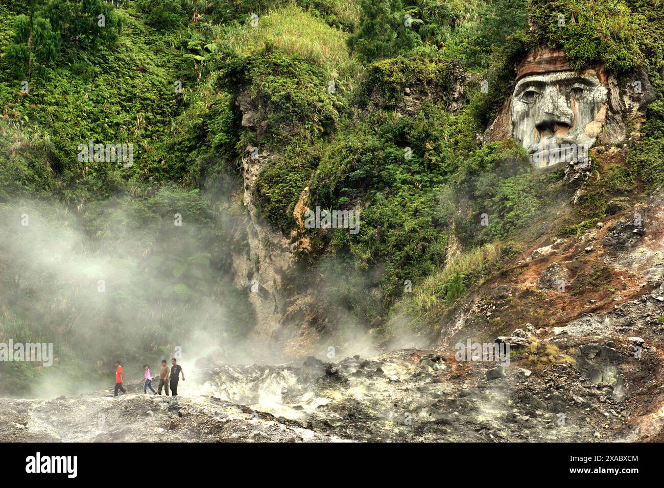 I visitatori hanno tempo libero sul campo delle fumarole, sotto l'arte scultorea che illustra il Toar (figura ancestrale) nel nord di Sulawesi, Indonesia. Foto Stock