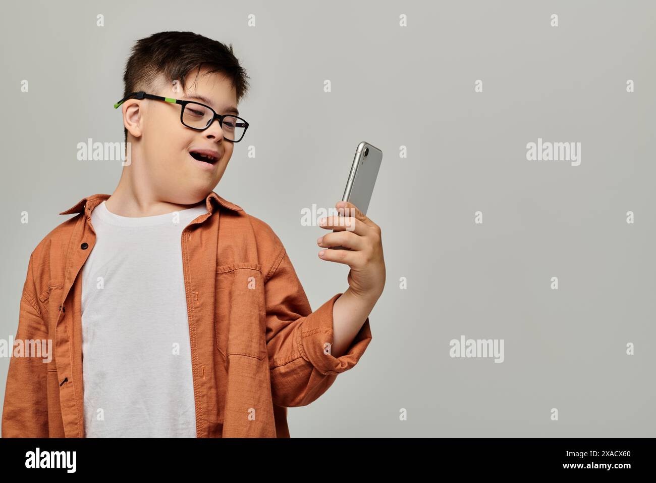 Un ragazzo con la sindrome di Down con gli occhiali ha un cellulare. Foto Stock