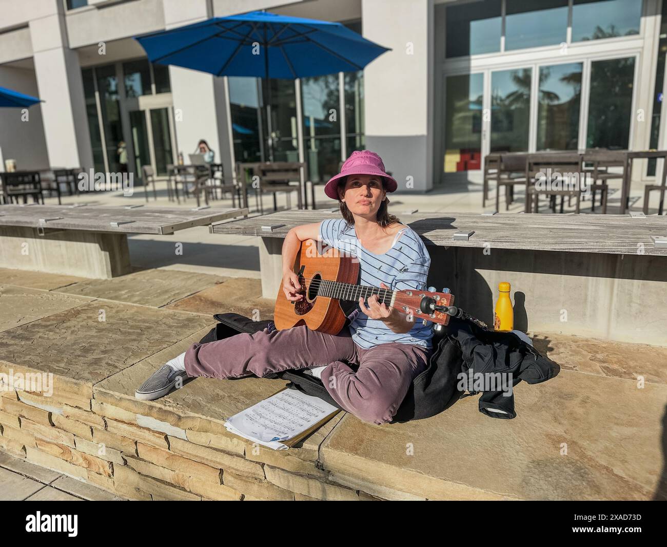 Santa Barbara, California, U.S.A. 4 giugno 2024. Tova Morrison di Santa Barbara suona e canta canzoni israeliane in ebraico sulla sua chitarra di fronte al Summit Cafe e alla biblioteca, come una pacifica e sottile contrapposizione contro il vicino accampamento offensivo e antisemita pro-Palestina sul campus UCSB il 3 giugno 2024, dopo che gli scioperanti dell'UAW hanno finito di picchettare per il secondo giorno del loro sciopero in questo stesso posto. Una palma proietta una lunga ombra in primo piano. (Immagine di credito: © Amy Katz/ZUMA Press Wire) SOLO PER USO EDITORIALE! Non per USO commerciale! Foto Stock