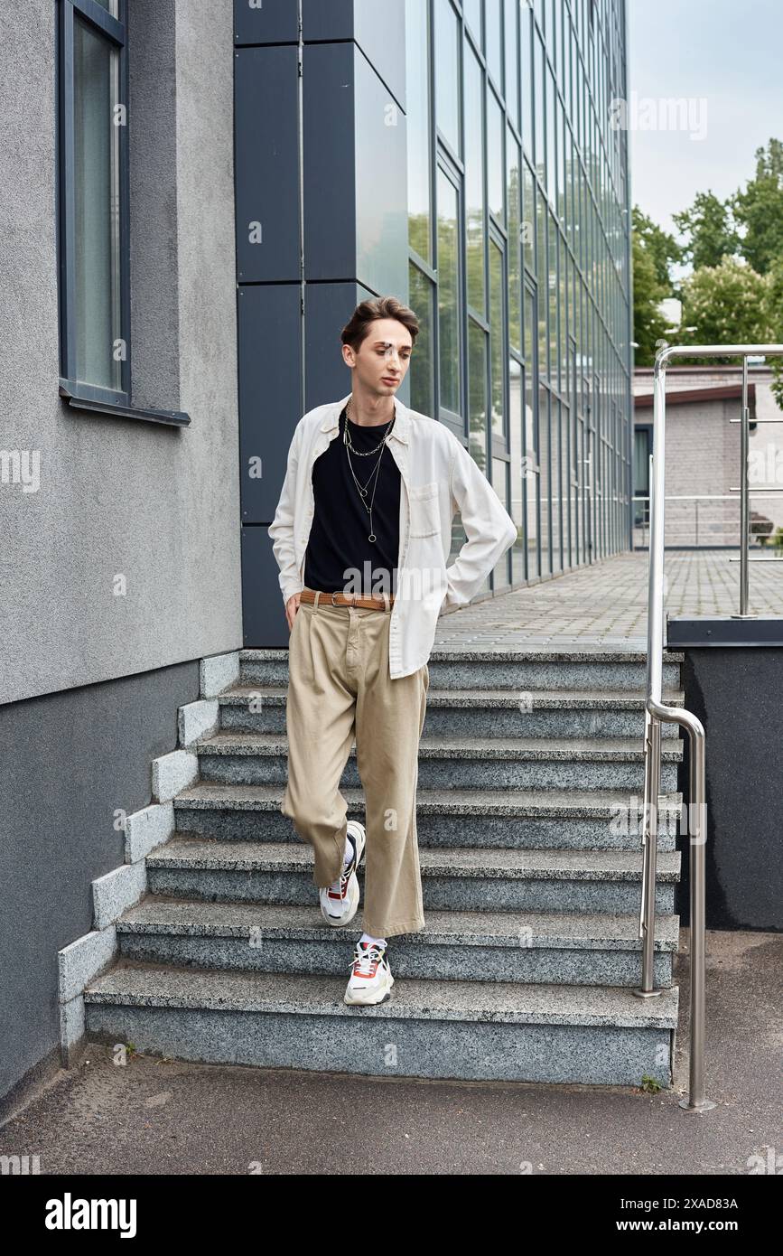 Un giovane queer, vestito con un abbigliamento elegante, si mette in posa sui gradini di un edificio. Foto Stock
