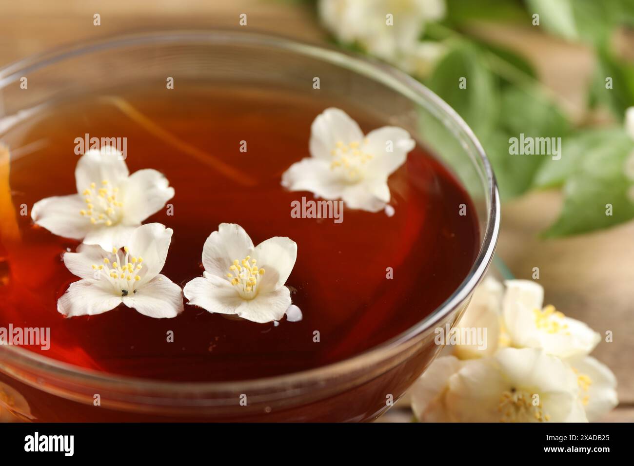 Tè caldo al gelsomino in tazza e fiori su tavola di legno, primo piano Foto Stock