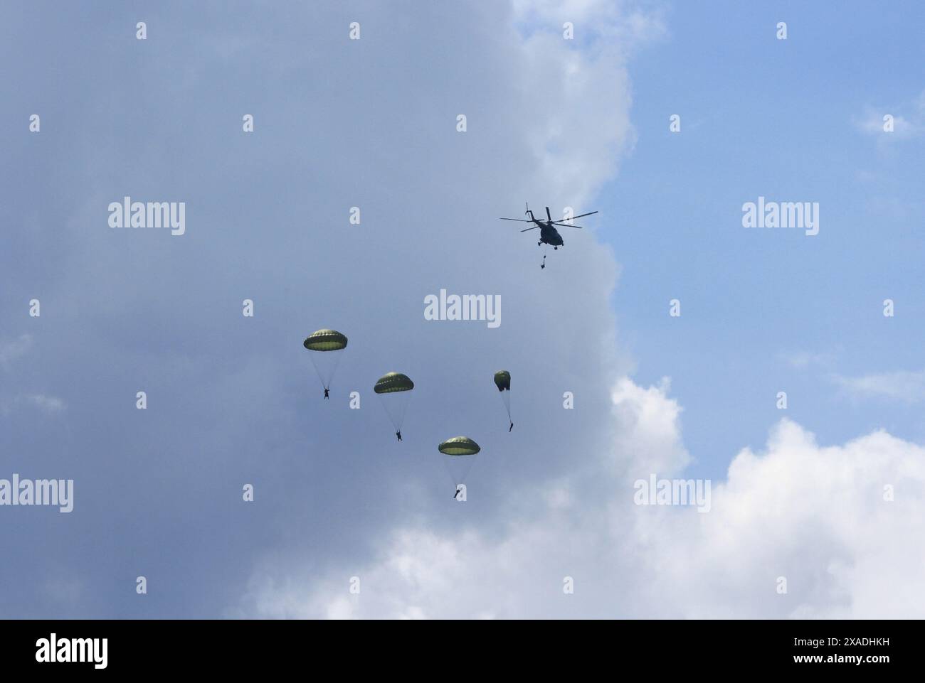 Cinque paracadutisti militari che saltano da un elicottero contro nuvole drammatiche, un paracadute si sta svolgendo, uno sta cadendo dall'elicottero Foto Stock