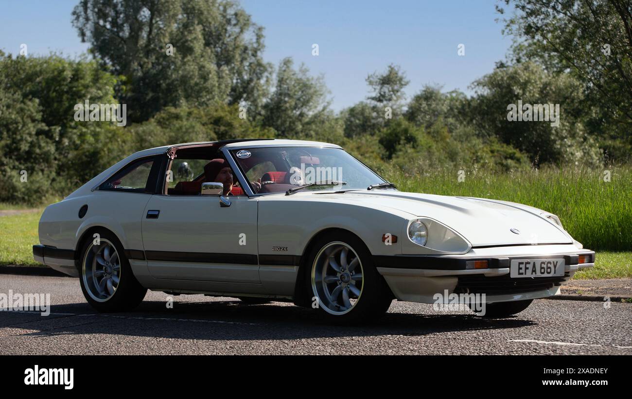 Stony Stratford, Regno Unito - 2 giugno 2024: 1983 Nissan 280 zx auto d'epoca bianca che guida su una strada di campagna britannica Foto Stock