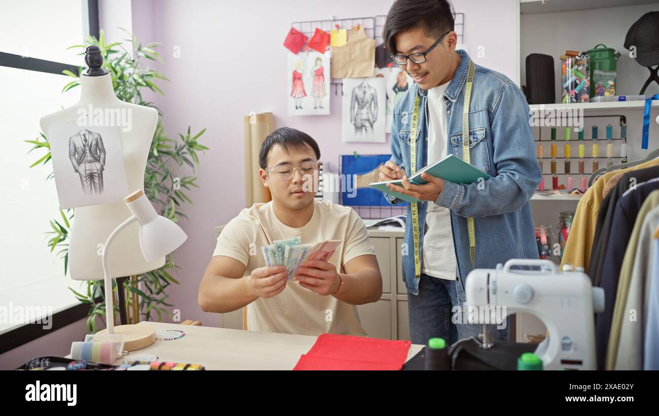 Due uomini che collaborano in un negozio di sartoria con uno che conta yuan e l'altro prende appunti tra schizzi di design e un manichino. Foto Stock