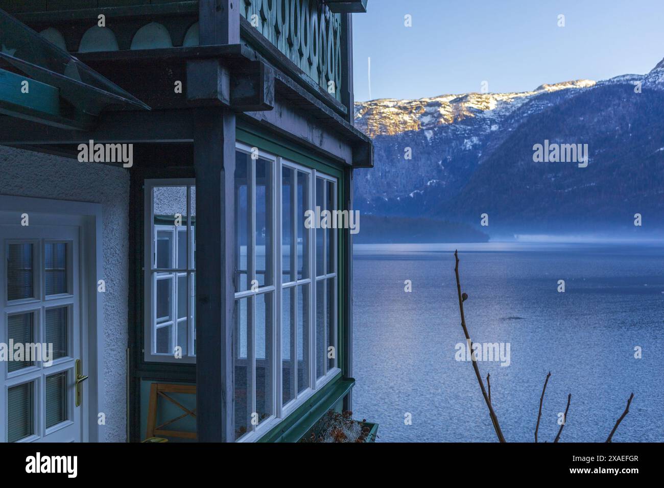 Fotografia di una casa bianca con balcone verde in legno sul lago alpino di Hallstatt al tramonto invernale Foto Stock