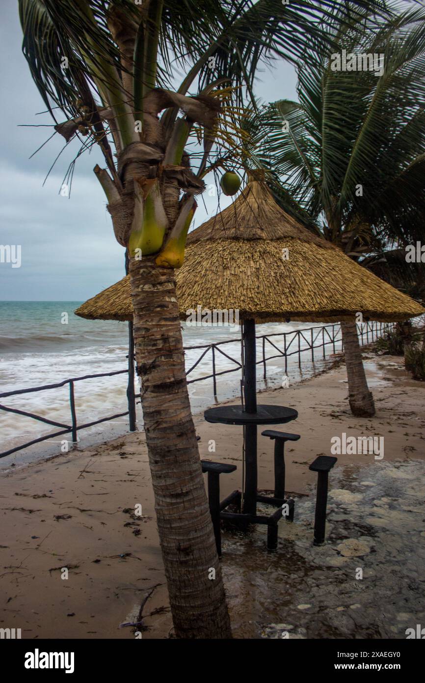 Un tavolino con sedie sotto un ombrellone di paglia, dopo un temporale sulla spiaggia di Inhassoro in Mozambico Foto Stock