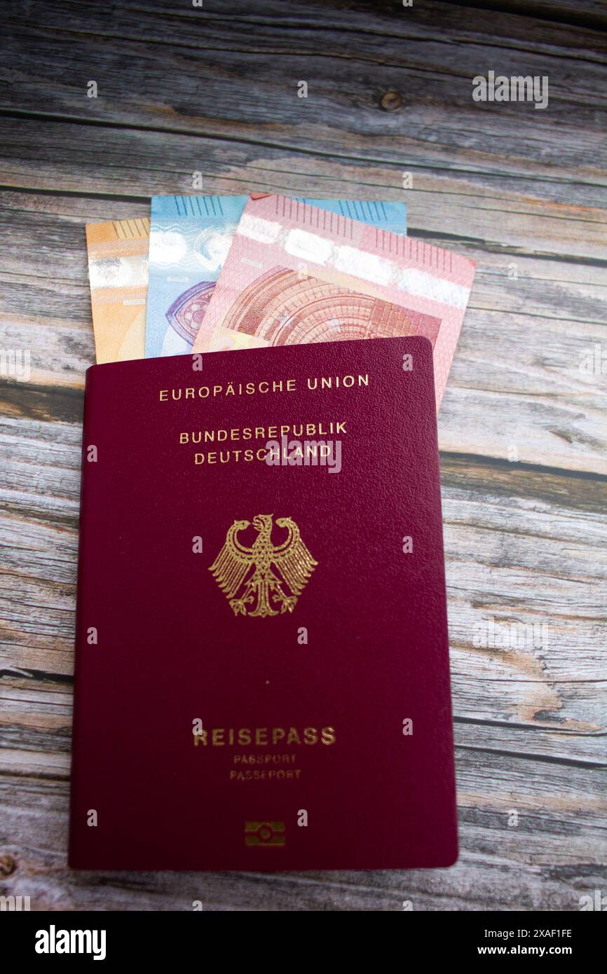 Foto verticale del passaporto di viaggio tedesco con le banconote in euro su sfondo di legno e le monete in euro su sfondo di legno Foto Stock