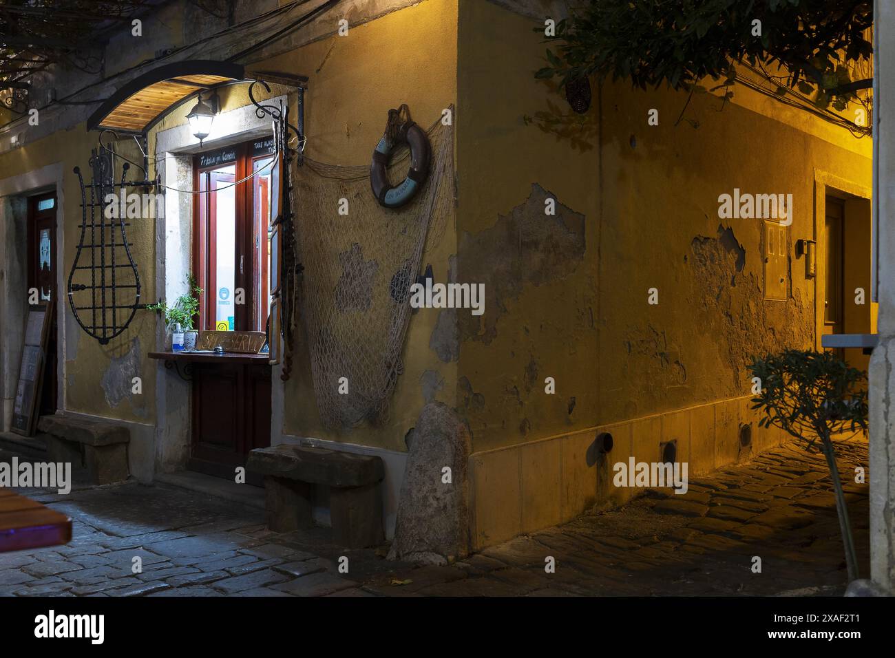 Foto di un vecchio edificio giallo con decorazioni da pesca nel centro della città costiera di Pirano in Slovenia, alla luce notturna Foto Stock