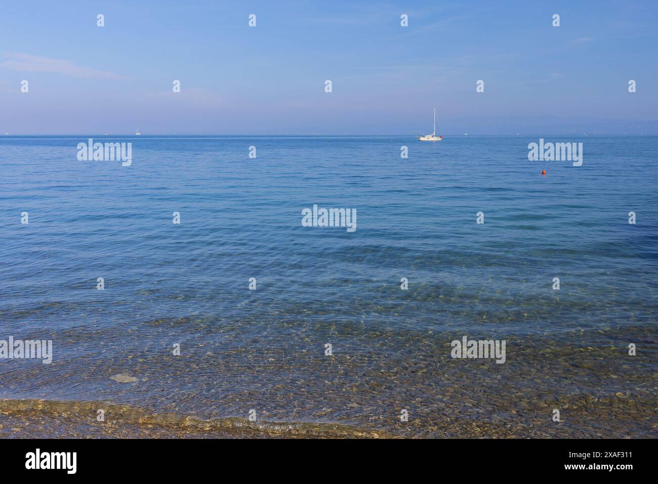 Foto panoramica del mare Adriatico con spiaggia di ciottoli e barca a vela bianca all'orizzonte sotto il cielo azzurro nella giornata di sole Foto Stock