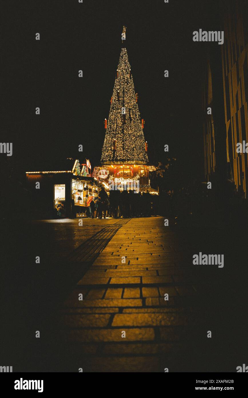 Un grande albero di Natale illuminato nel centro di un festoso mercatino di Natale tedesco di notte Foto Stock