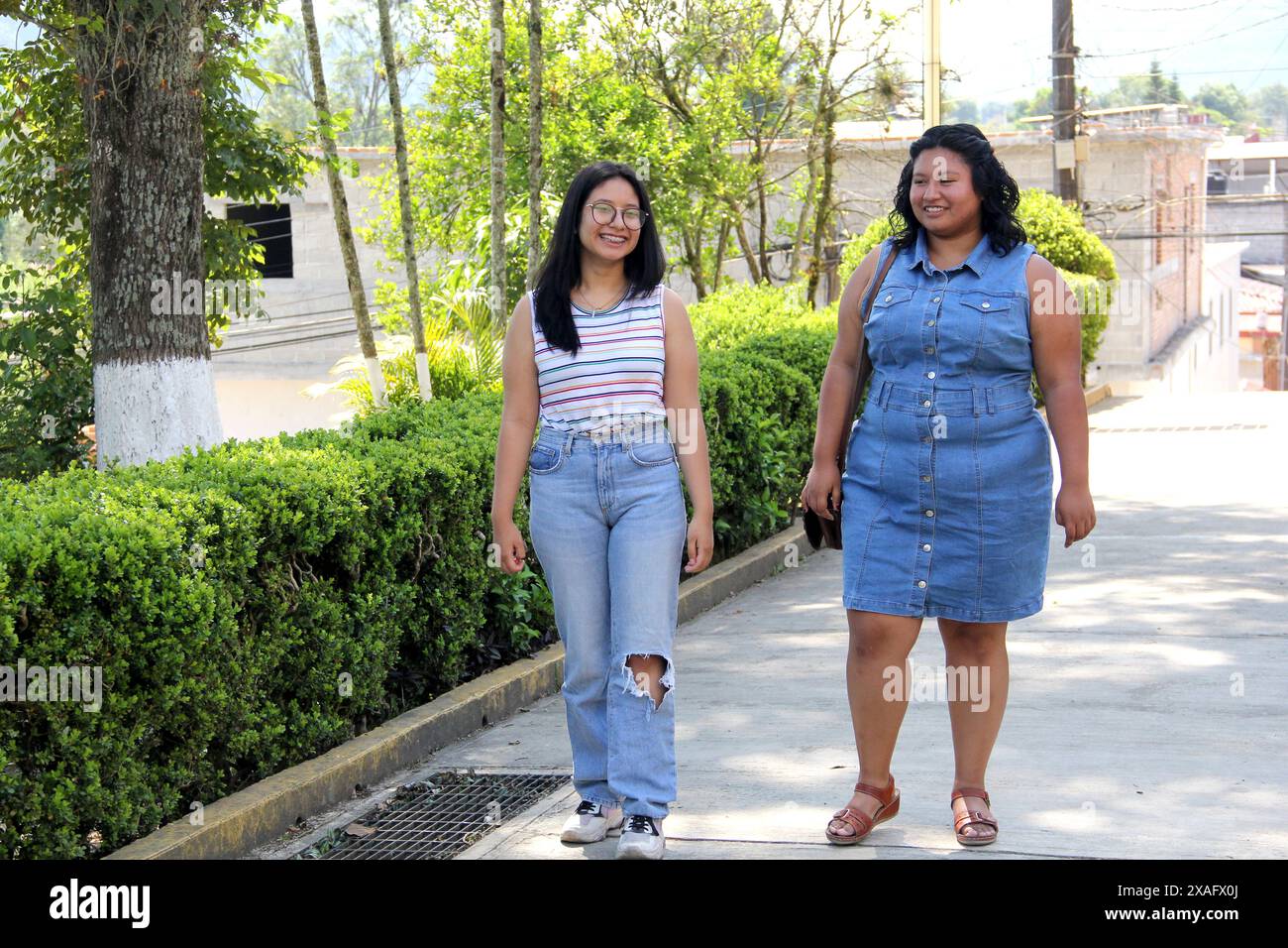 Due giovani donne sorelle e brune amiche latine camminano e parlano nel parco trascorrono del tempo insieme dopo la scuola Foto Stock