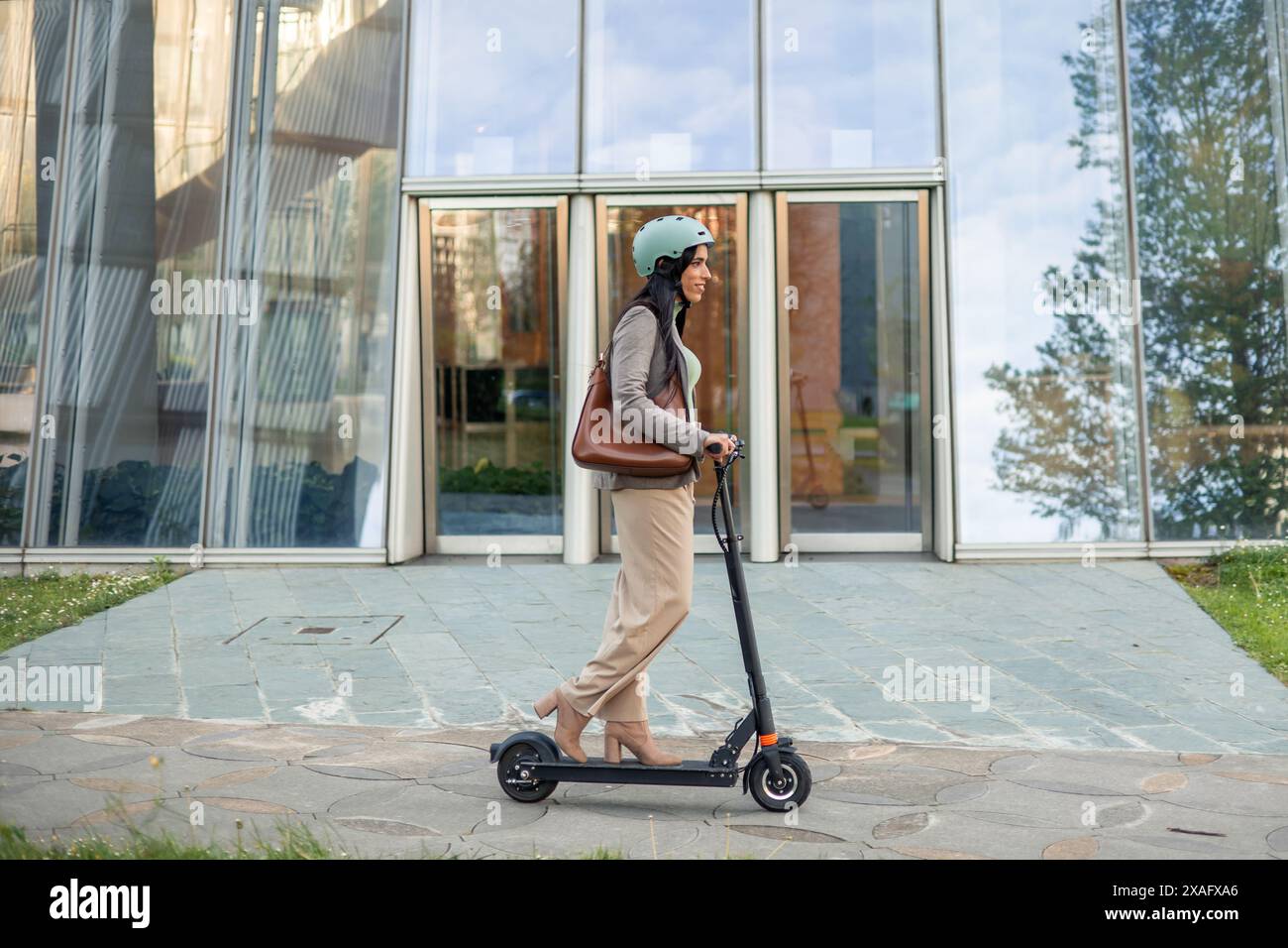 una donna d'affari è vista spostarsi verso il proprio posto di lavoro in modo ecologico e rispettoso dell'ambiente, utilizzando uno scooter elettrico per un Foto Stock