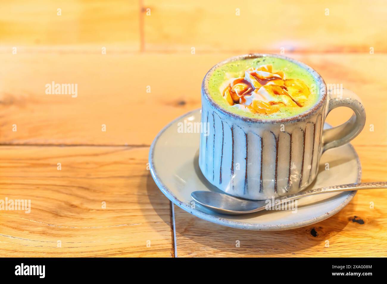 Un latte di tè verde matcha giapponese frizzante servito in una tazza di ceramica rustica con un cucchiaio, adornato con panna montata e un filo di caramello, siede inviti Foto Stock