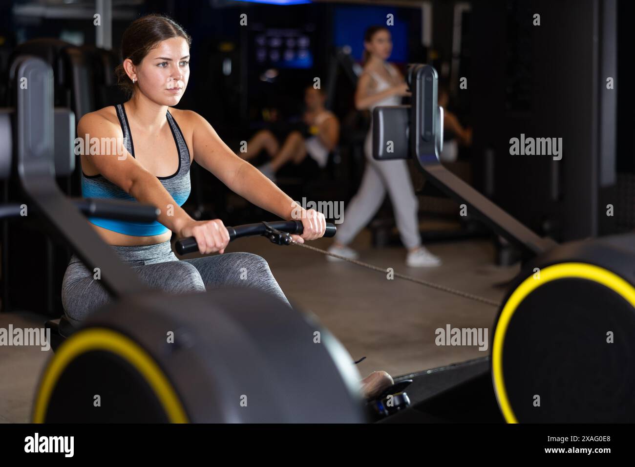 La ragazza esegue esercizi con la macchina per remare in palestra Foto Stock