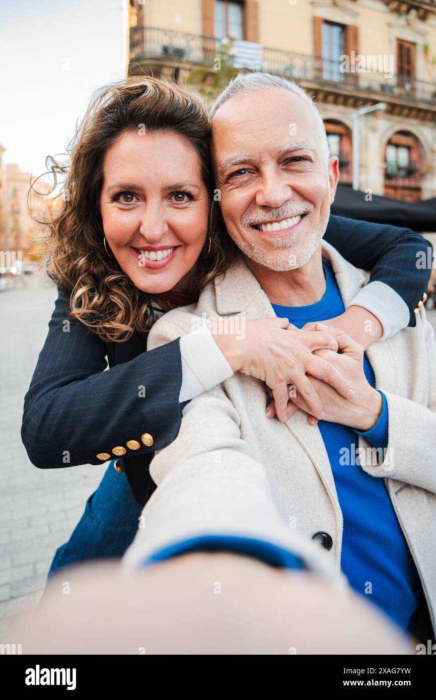 Verticale. coppia matura in una relazione che sorride e guarda la telecamera. Donna adulta che abbraccia il suo marito di capelli grai e si lega all'esterno. Le persone sposate di mezza età si godono un abbraccio affettuoso. Foto di alta qualità Foto Stock