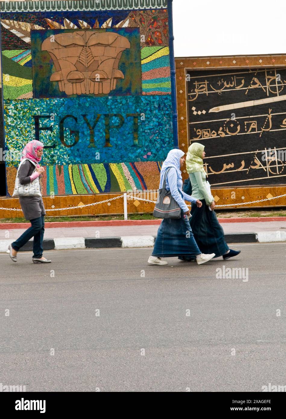 Studenti universitari egiziani che camminano accanto a un muro decorato con colori ad Alessandria, in Egitto. Foto Stock