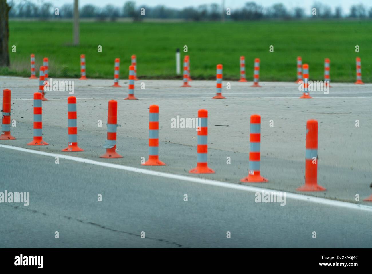 Una fila di coni stradali arancioni e bianchi è allineata su una strada. I coni sono distanziati e non sono in uso Foto Stock