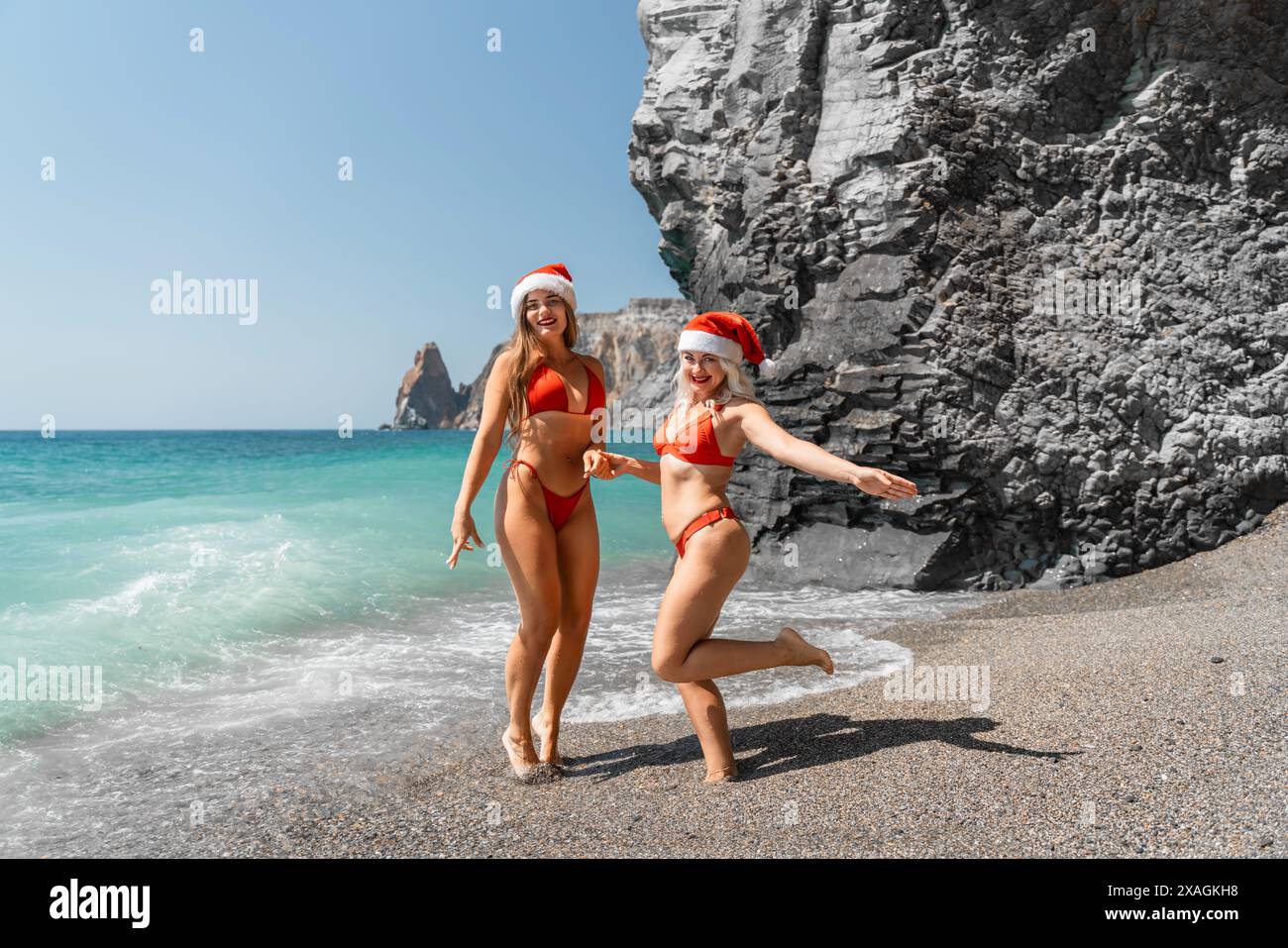 Le donne con i cappelli di Babbo Natale si imbattono nel mare vestite di costumi da bagno rossi. Festeggiamo il nuovo anno in un paese caldo. Foto Stock