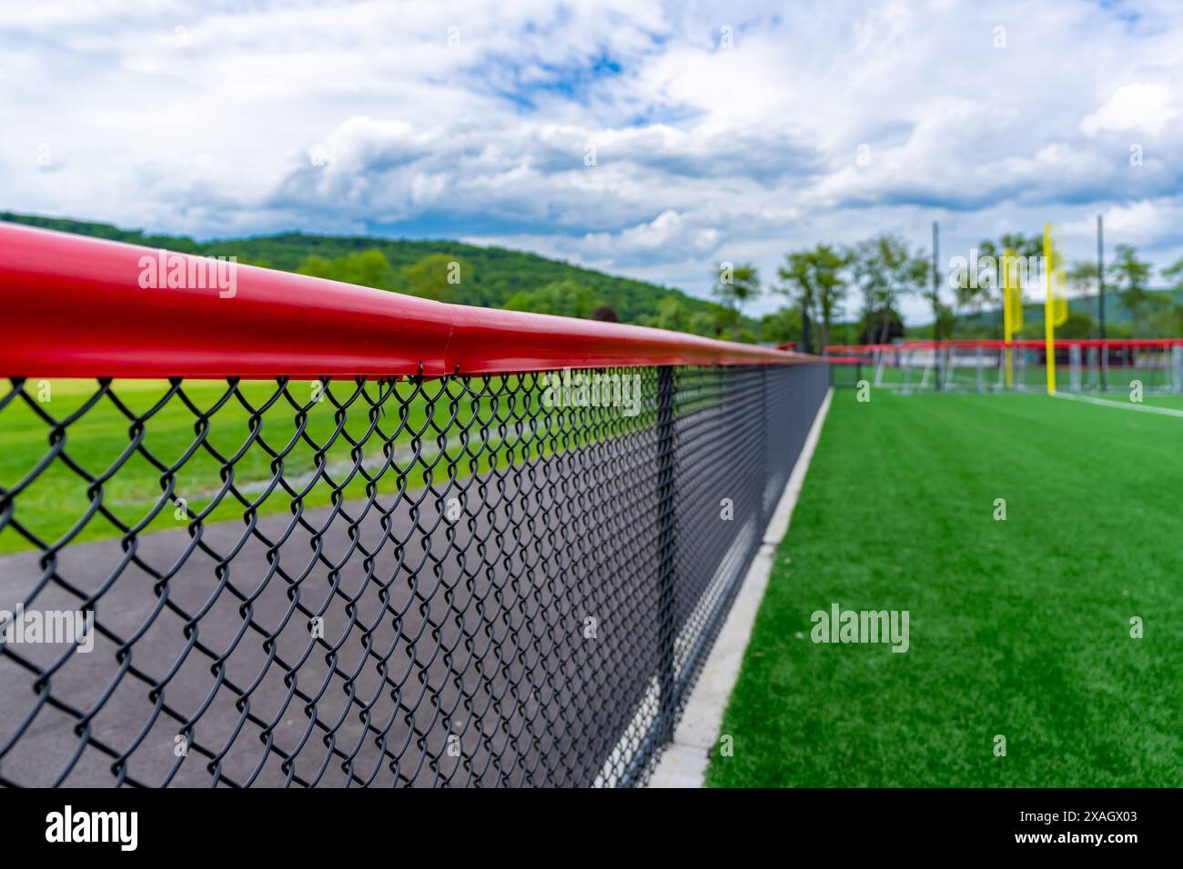 Recinzione nera a maglie con cappellino rosso e campo sportivo da softball/baseball sullo sfondo. Foto Stock