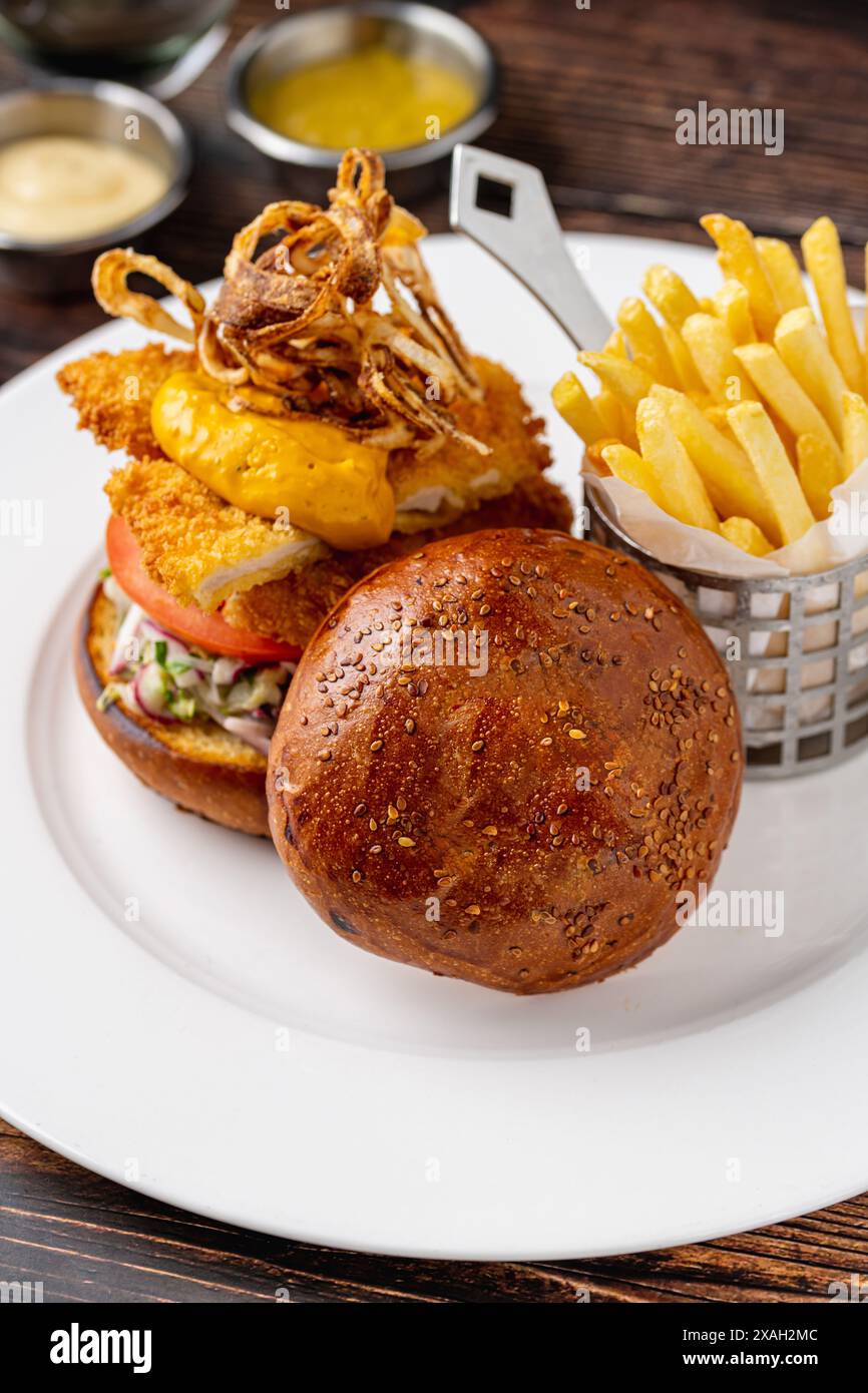 Hamburger di pollo servito con patatine fritte e salse su un piatto di porcellana bianca Foto Stock