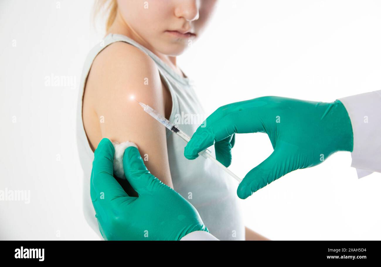 Le mani di un medico in guanti medici verdi fanno una vaccinazione contro la difterite, pertosse e tetano nella spalla di una bambina. Copia Foto Stock
