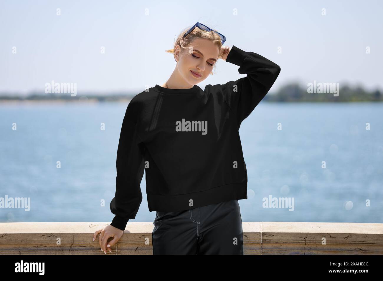 Mockup di una felpa nera su una bella ragazza con il sole, sullo sfondo di un fiume, molo, vista frontale. Modello streetwear da donna con lo Foto Stock