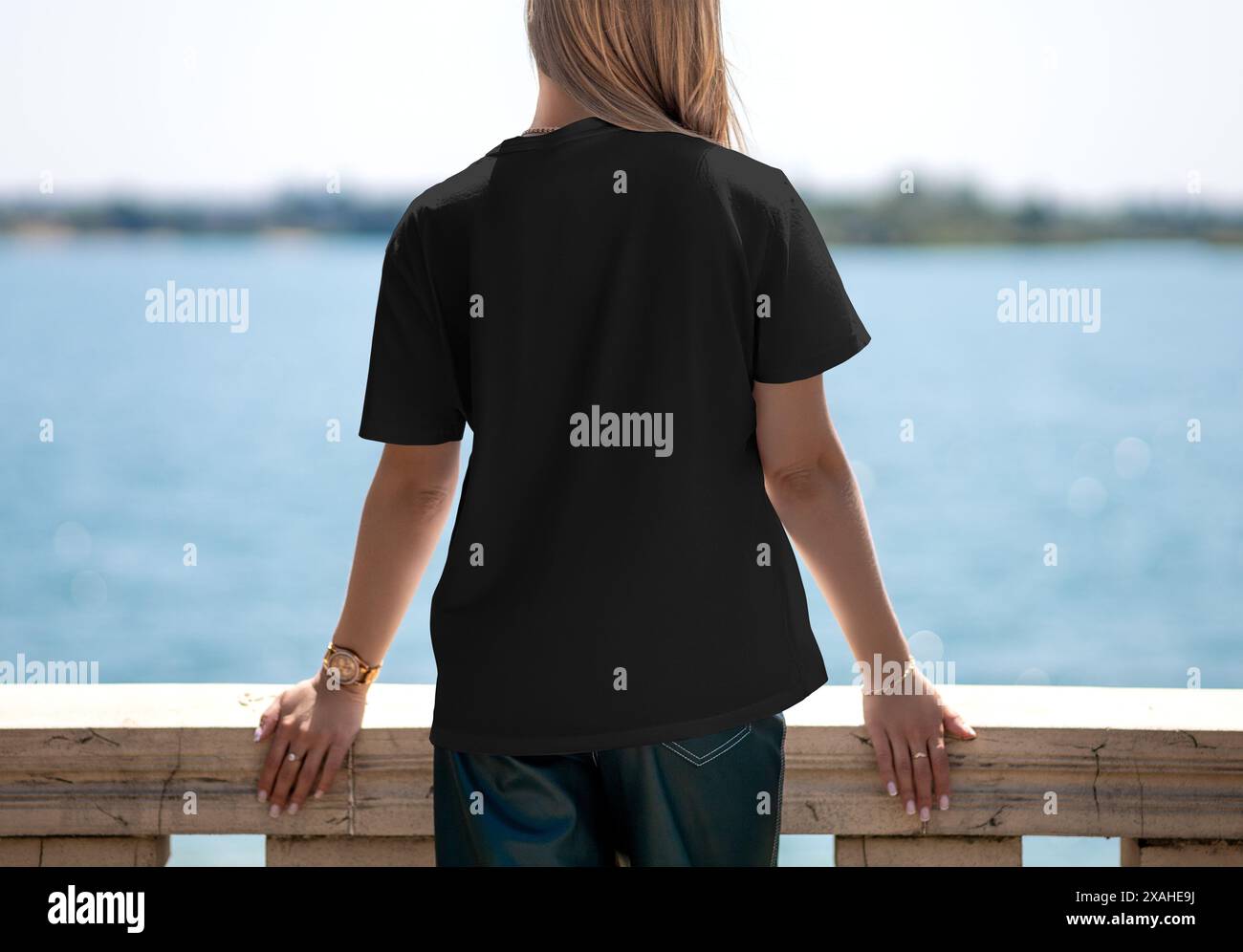 Modello di T-shirt nera su una ragazza bionda sullo sfondo di un fiume, vista posteriore, per design, branding, pubblicità. Mockup di moda Foto Stock