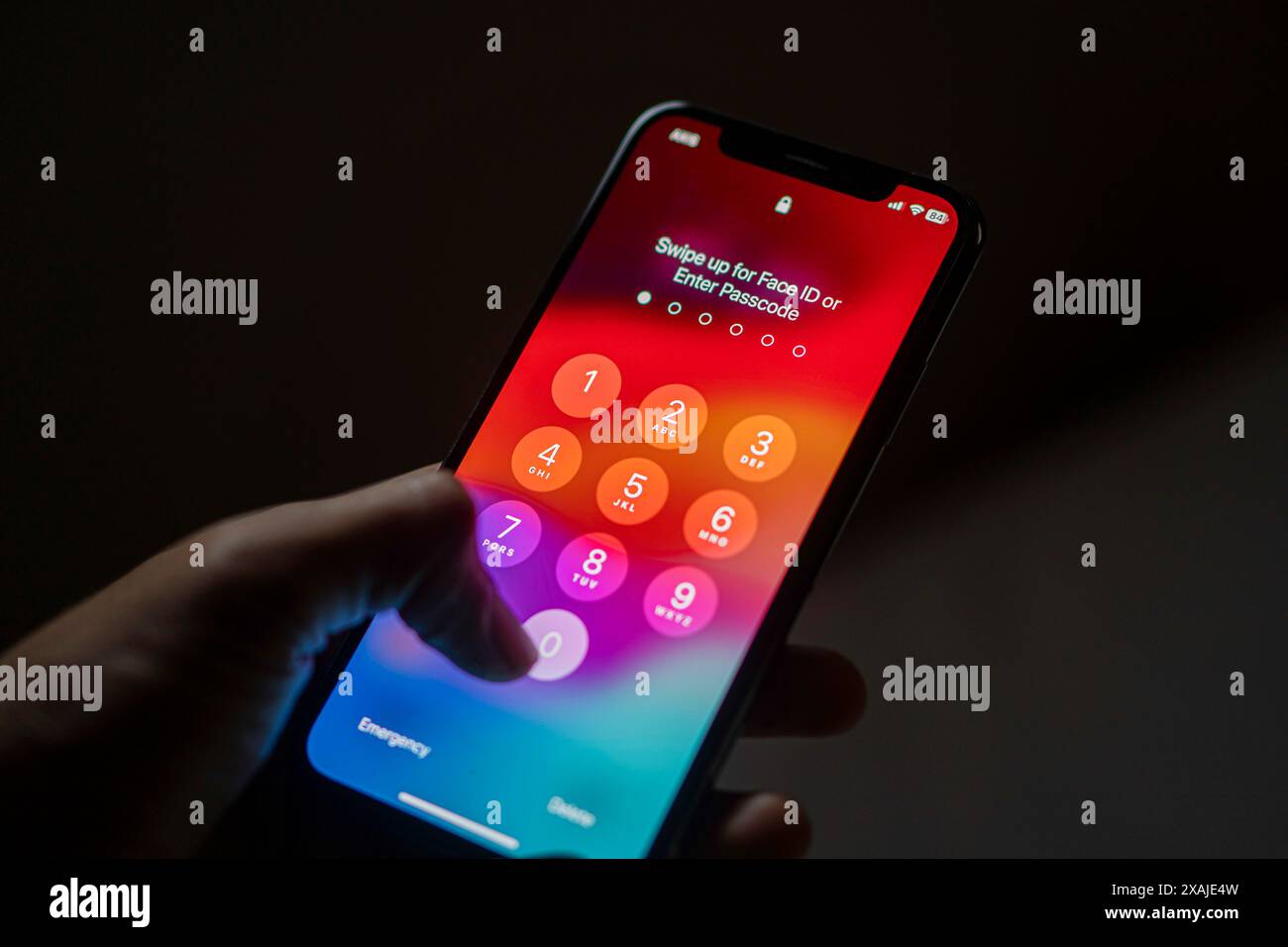 Una persona che possiede uno smartphone con una schermata codice di accesso visualizzata, che indica la necessità di immettere un codice di accesso o utilizzare il Face ID per sbloccare il dispositivo. Foto Stock