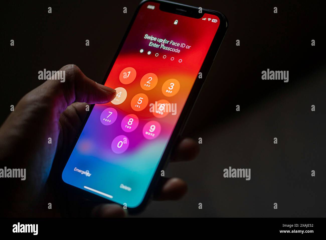 Una persona che possiede uno smartphone con una schermata codice di accesso visualizzata, che indica la necessità di immettere un codice di accesso o utilizzare il Face ID per sbloccare il dispositivo. Foto Stock