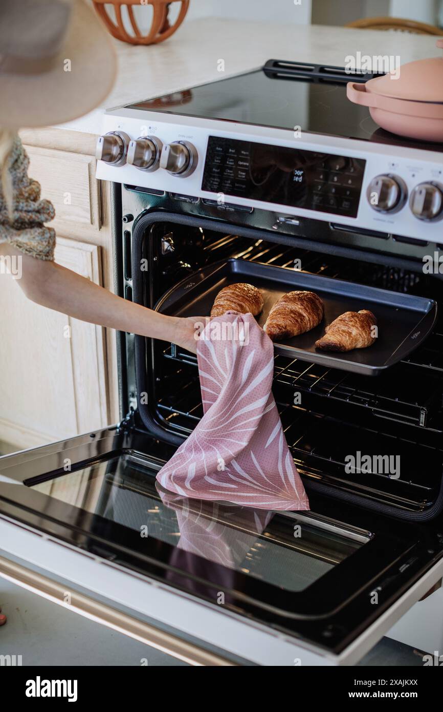 Donna che prende dal forno un vassoio di croissant appena sfornati Foto Stock