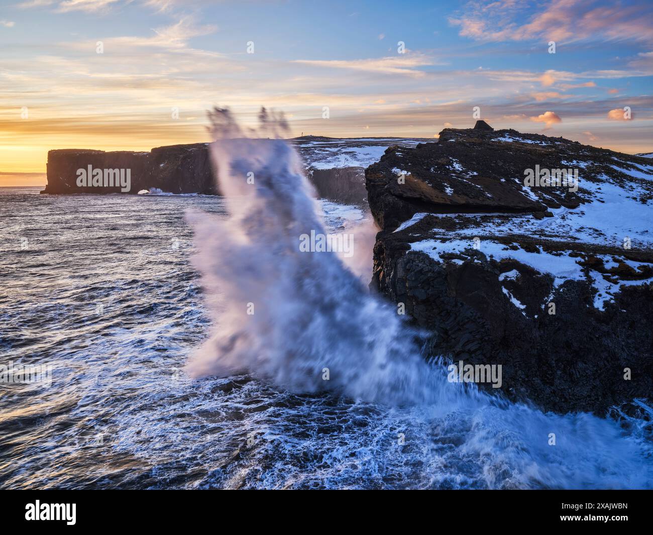 Al crepuscolo invernale, le scogliere lungo la costa della penisola di Dyrholaey sono incessantemente lambite Foto Stock