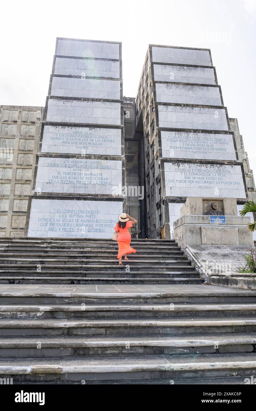 Nord America, Caraibi, isola Hispaniola, Repubblica Dominicana, Santo Domingo, donna in abito estivo arancione davanti al faro a Colon Foto Stock