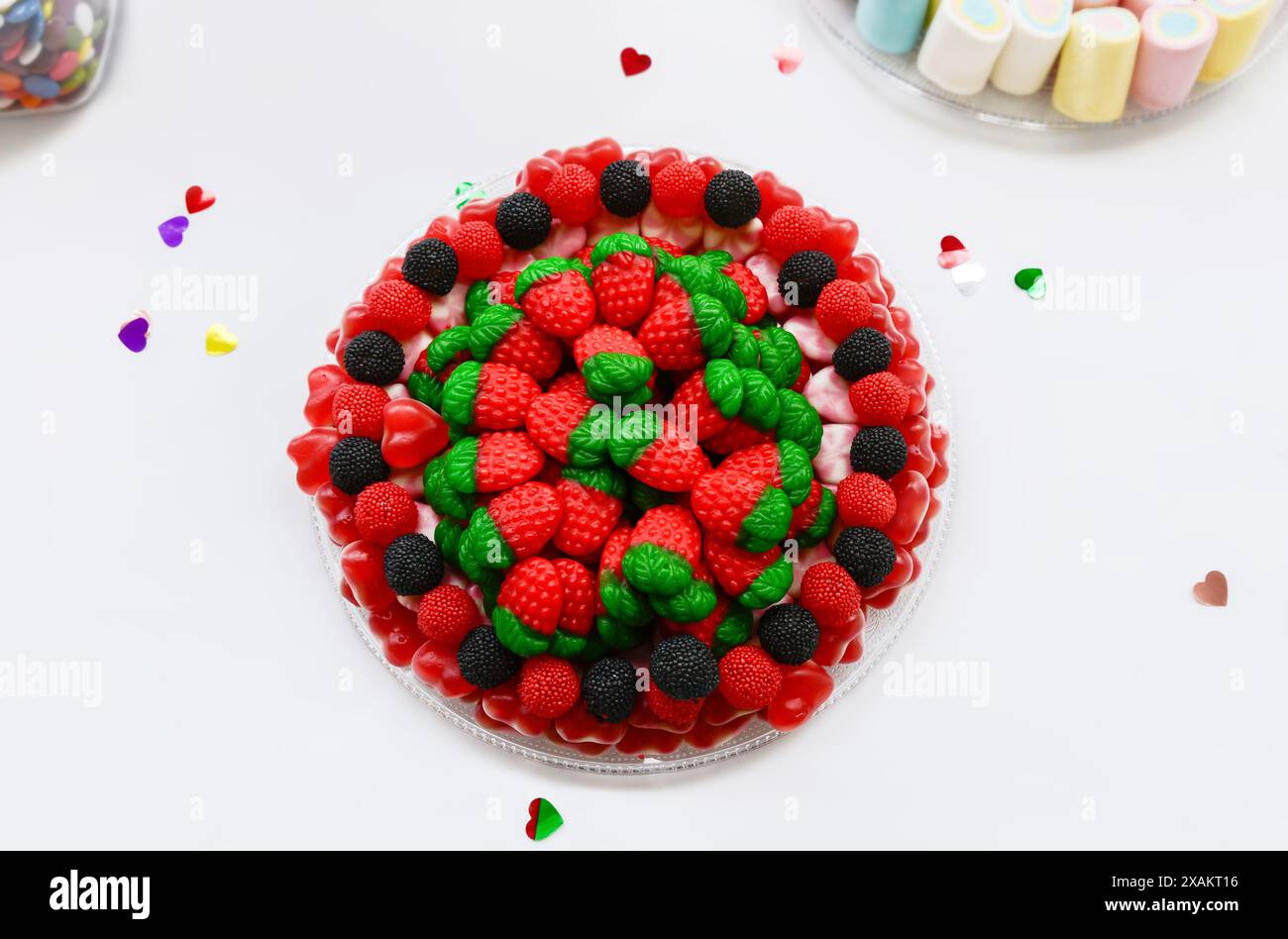 Vista dall'alto di gustosi dolci in gelatina a forma di fragole rosse e di more nere e rosse su un piatto su sfondo bianco. Foto Stock Vista dall'alto di gustosi dolci in gelatina a forma di fragole rosse e di more nere e rosse su un piatto su sfondo bianco. Foto Stock