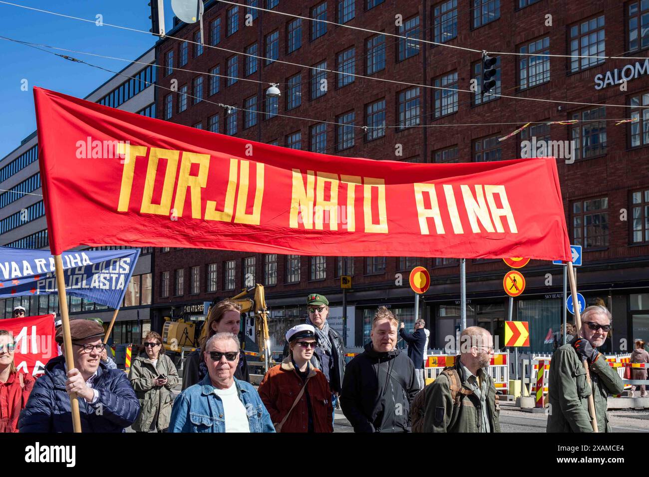 Torju NATO aina. Manifestanti che portano striscione rosso alla marcia del Labor Day su Siltasaarenkatu nel distretto di Hakaniemi di Helsinki, Finlandia. Foto Stock