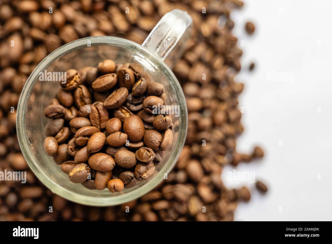 Una tazza da caffè trasparente cosparge di chicchi appena tostati, evocando l'aroma di un caffè perfetto. Foto Stock