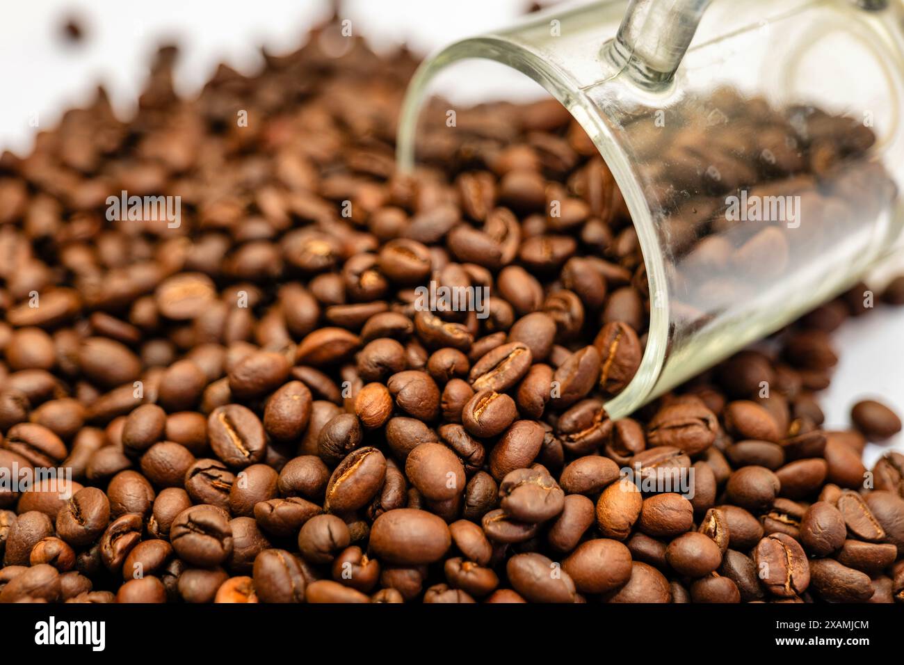 Vista ravvicinata dei chicchi di caffè appena tostati che fuoriescono da una tazza di vetro, evocando calore e gioia dei rituali mattutini. Foto Stock